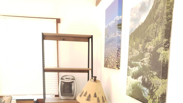 Una habitación pequeña con una cama, un escritorio con lámpara, un radiador y una ventana con persianas.