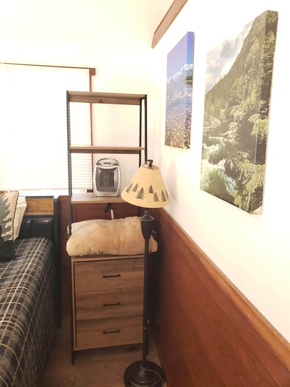 Una habitación pequeña con una cama, un escritorio con lámpara, un radiador y una ventana con persianas.