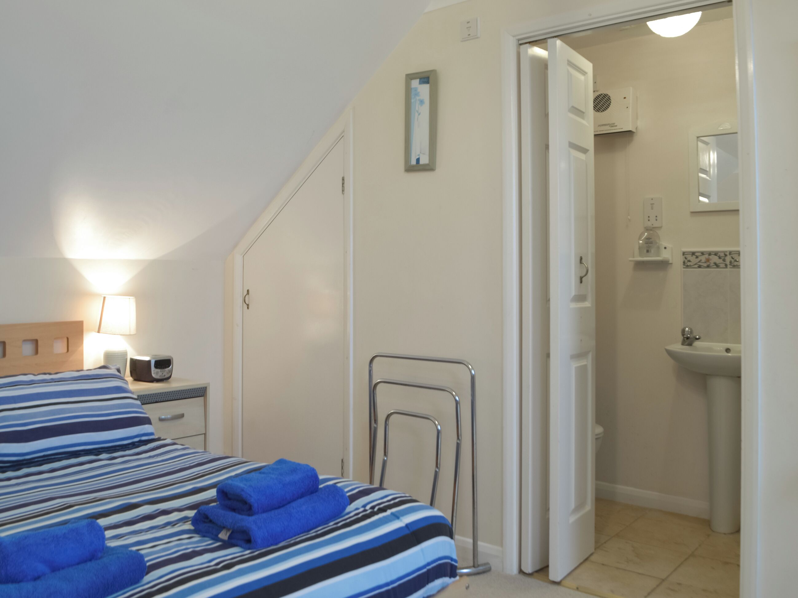 Une chambre d’hôtel comprenant un lit, une table de chevet avec une lampe, un radiateur et une salle de bain avec un lavabo et un miroir.