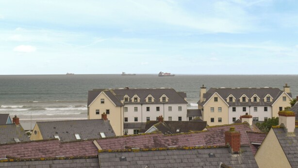 Un pueblo costero con casas tradicionales, vista al mar y barcos a lo lejos.