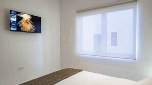 A hotel room with a bed, a television mounted on the wall, and a window with blinds.