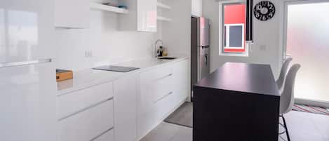 Une cuisine moderne avec des meubles blancs, un îlot central doté d’un plan de travail noir et un réfrigérateur en acier inoxydable.
