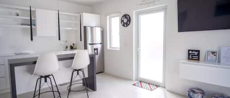 A modern kitchen with a central island, two bar stools, a refrigerator, and a wall-mounted clock.