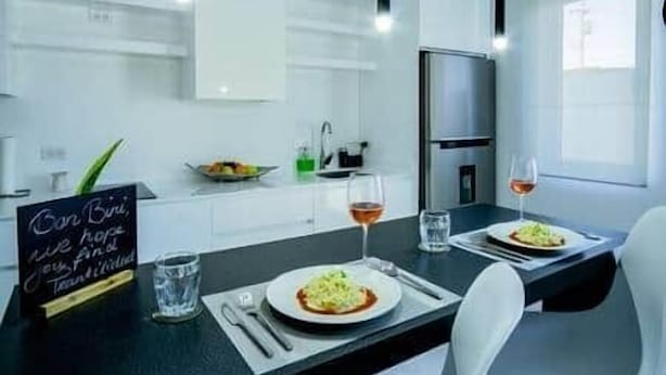 A modern kitchen with white cabinets, a black countertop, and a dining area with two plates of food and glasses of wine.