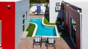 A modern pool area with a rectangular pool, two lounge chairs, and a small table.