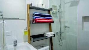 A bathroom with a glass shower enclosure, a white sink, and a shelf with folded towels.
