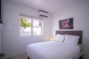 Ein Hotelzimmer mit Bett, Fenster, Klimaanlage, einem Wandbild und einer Nachttischlampe.