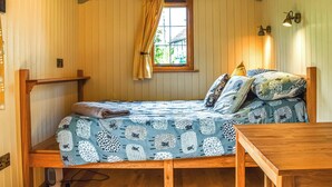 Um quarto aconchegante com uma cama, uma mesinha de cabeceira de madeira, uma janela com cortinas e um aparelho de luz fixado na parede.