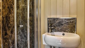 Casa de banho com chuveiro em compartimento de mármore e lavatório branco com painel de apoio em mármore.