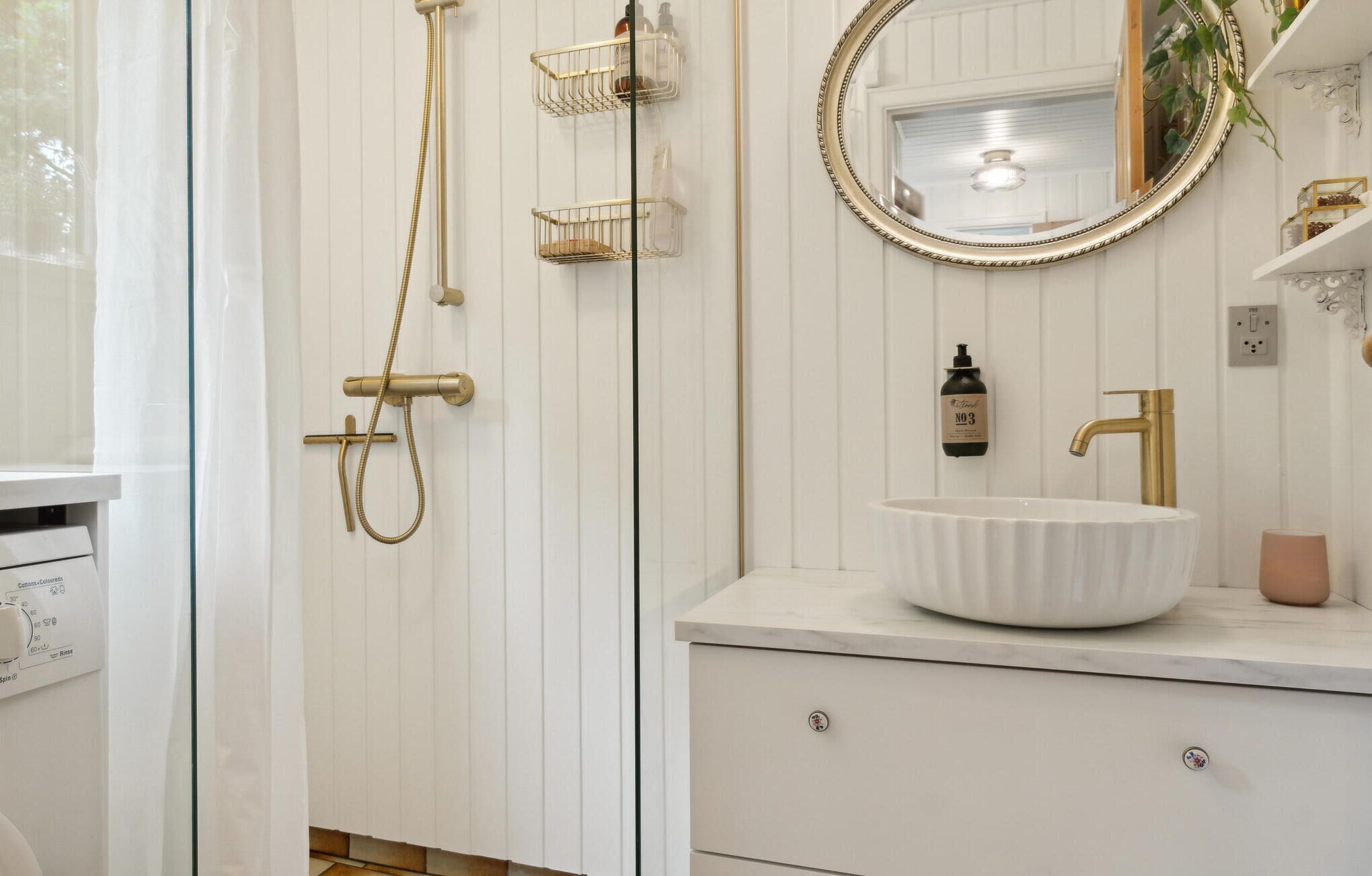 Une salle de bain avec un lavabo blanc, des robinetteries dorées et un miroir avec un cadre doré.