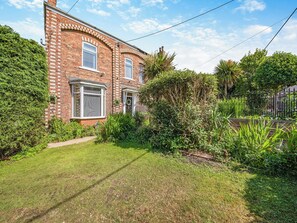 A brick house with a well-maintained garden, a paved driveway, and a metal fence.
