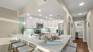 Una cocina moderna con armarios blancos, electrodomésticos de acero inoxidable y una isla central con taburetes de bar.