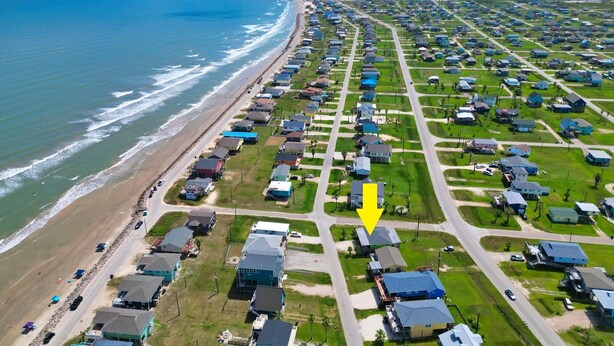 An aerial view of a coastal residential area with houses arranged in a grid pattern, a beach to the left, and a clear sky. - Spacious beach bungalow 1 block from the ocean, 4 bedrooms (Freeport)