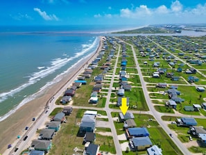 Vue aérienne d’un quartier résidentiel situé sur la côte, avec des maisons disposées selon un plan en forme de grille, une plage sur la gauche et un ciel dégagé.