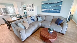 A modern living room with a sectional sofa, wooden coffee table, and a large abstract painting. - Spacious beach bungalow 1 block from the ocean, 4 bedrooms (Freeport)