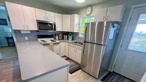 A modern kitchen with white cabinets, a stainless steel refrigerator, a microwave, and a stove. - Spacious beach bungalow 1 block from the ocean, 4 bedrooms (Freeport)