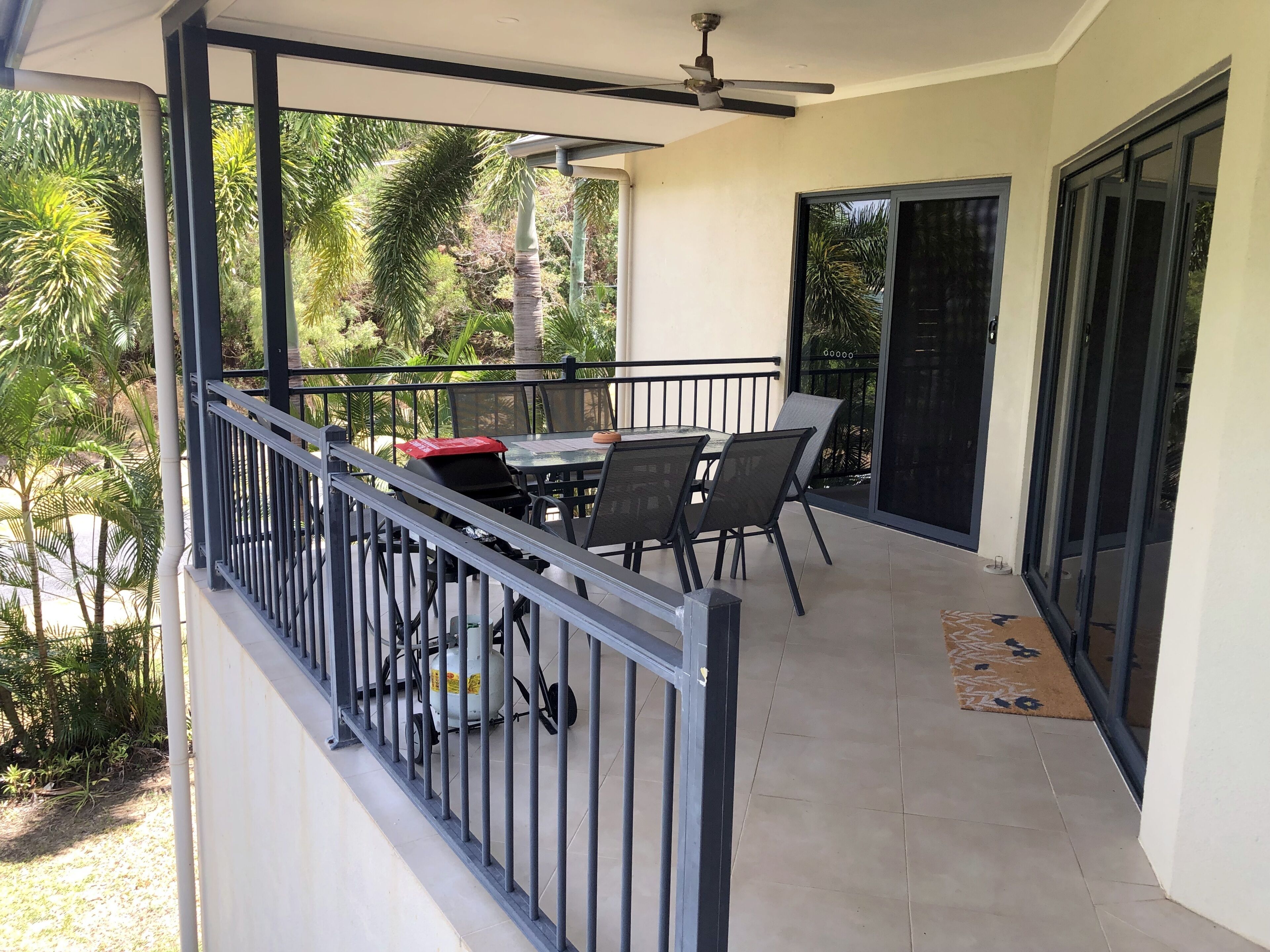 Un balcone con tavolo e sedie, una ventola a soffitto e vista su palme.