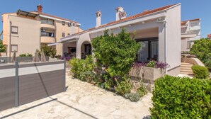 Une maison moderne à deux étages, dotée d’un chemin en pierre, d’un espace extérieur aménagé pour s’asseoir et d’un jardin.