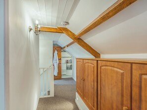 Un pasillo con vigas de madera, una puerta blanca y una escalera que conduce a una habitación con un armario de madera y una estantería.