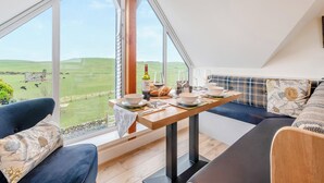 Un coin repas avec une table dressée pour deux personnes, une bouteille de vin et une vue pittoresque sur des champs et des collines verdoyants.
