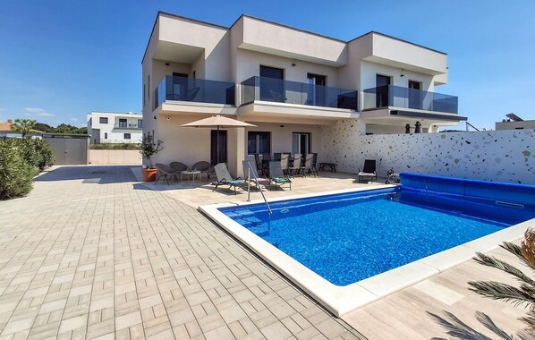 A modern two-story building with a swimming pool, outdoor seating, and a clear sky.