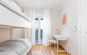 A bedroom with a bunk bed, a desk, a chair, and a window with curtains.