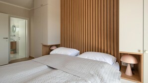Een moderne slaapkamer met een groot bed, een wand van houten panelen, bedlampen en een zichtbare badkamers deur.