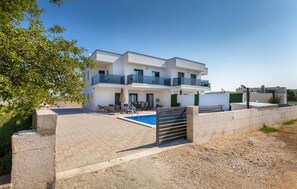 A modern two-story house with a swimming pool, outdoor seating, and a gated entrance.