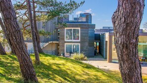 Una moderna casa a due piani con una scala a vista che conduce al piano superiore, immersa tra alberi e un'area verde.