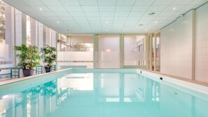 Una piscina con acqua cristallina, circondata da ampie finestre e piante in vaso.