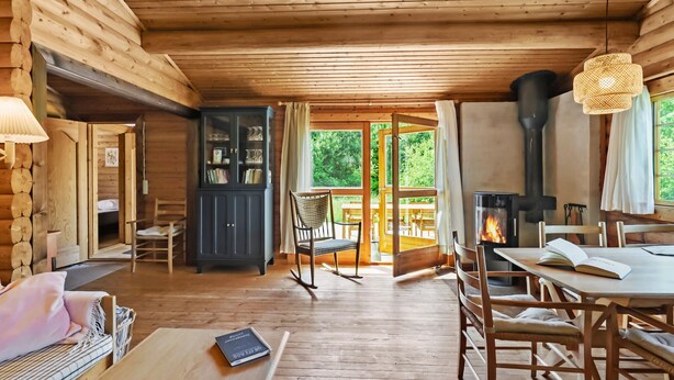 A cozy log cabin interior with a dining area, a rocking chair, and a fireplace. - Lovely home in Højslev with kitchen (Højslev)