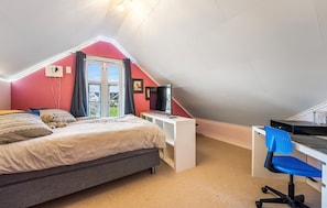 Un dormitorio con techo inclinado, una cama, un escritorio con silla y un televisor.