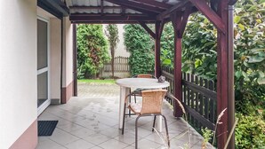 A covered patio with a table and chairs, a wooden fence, and greenery. - Nice apartment in Klucze with WiFi (Klucze)