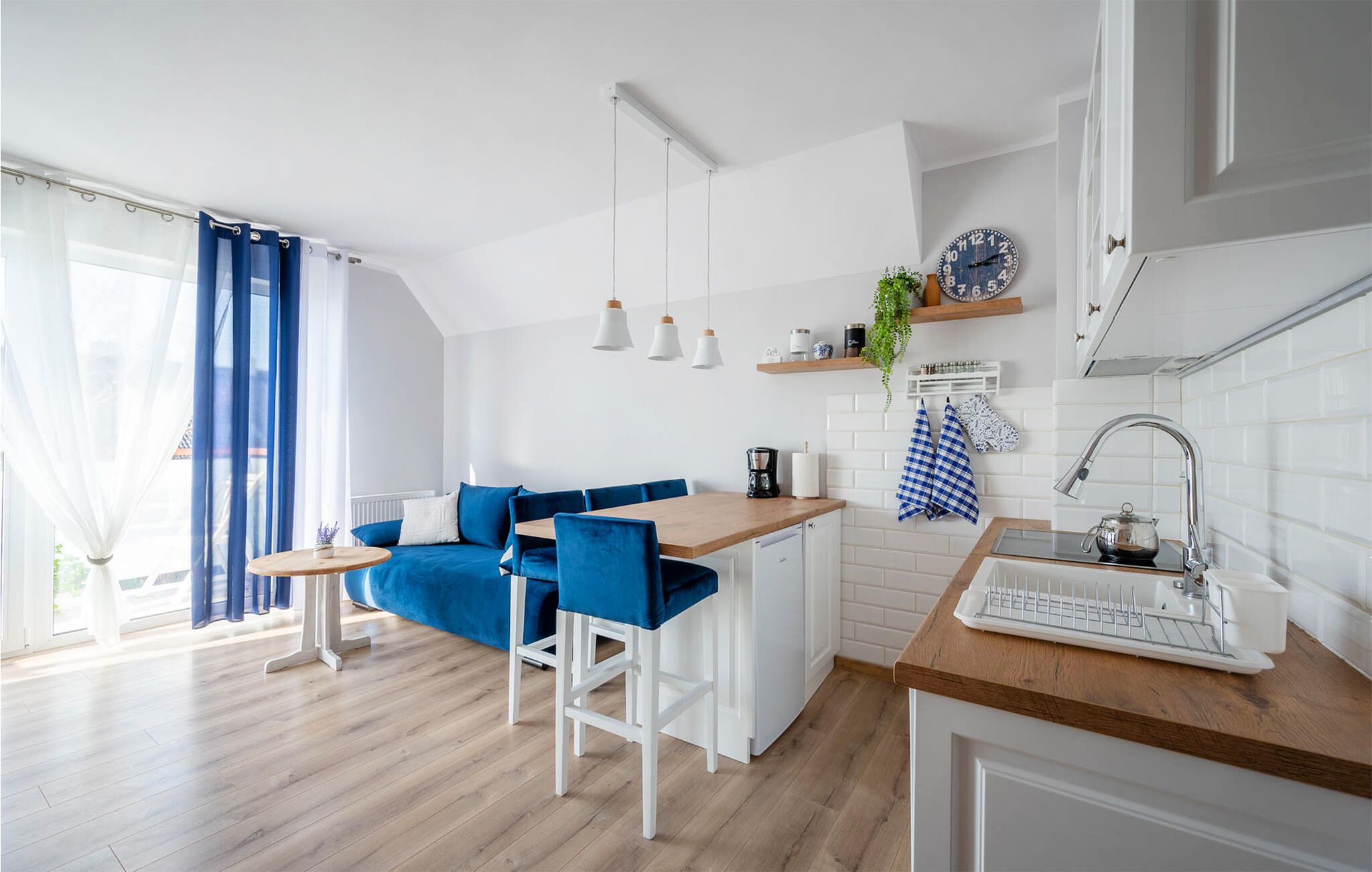 Een moderne keuken met een houten aanrecht, witte kastjes en blauwe barkrukken.