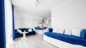 A modern, compact living space with a blue sofa, a small round table, and a kitchenette. - 1 bedroom beach front apartment in Darlówko (Darlówko)