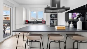Eine moderne Küche mit einer großen Kochinsel, Barhocker, einer Kaffeemaschine und Blick ins Freie.