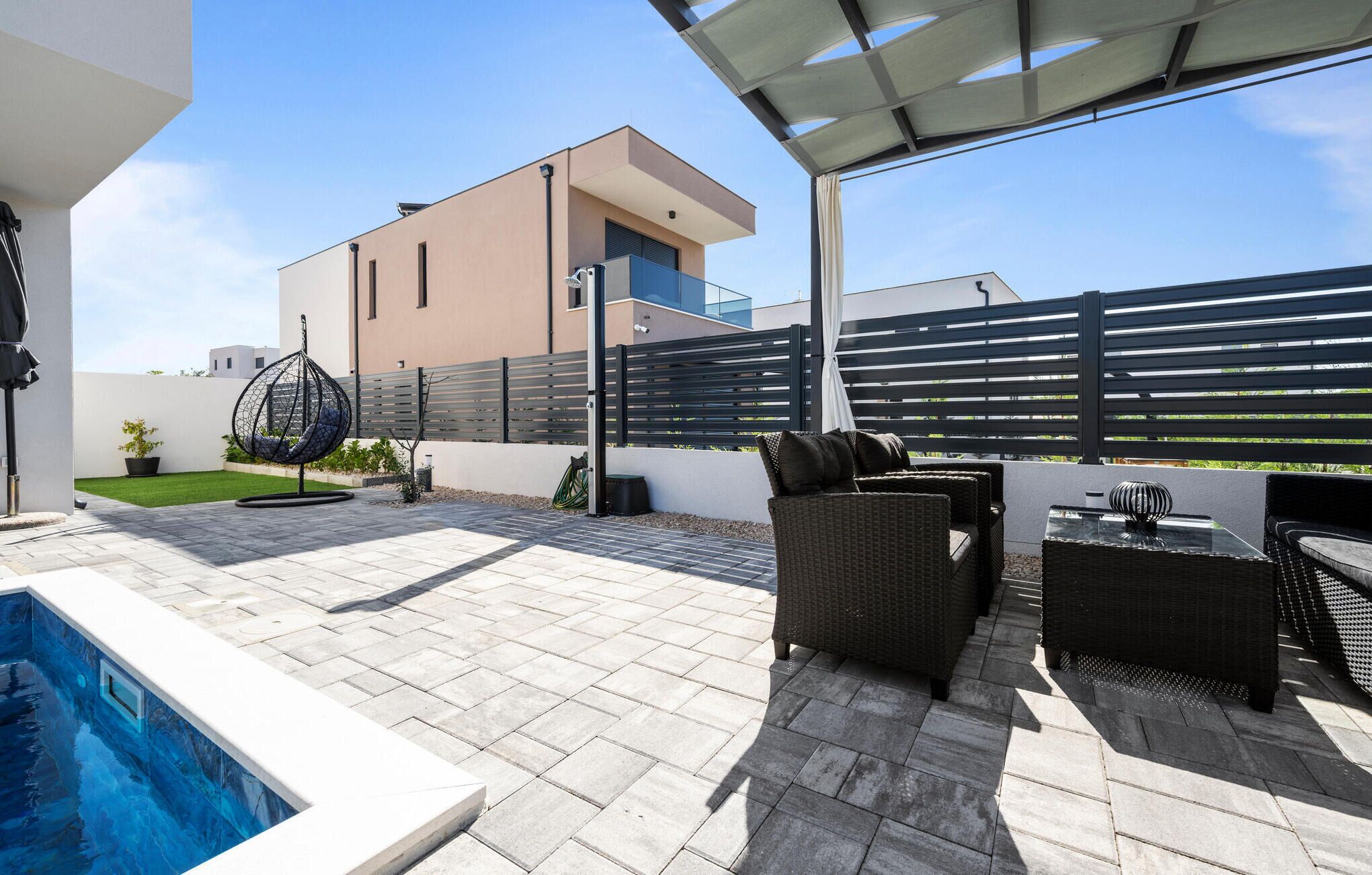 Eine moderne Terrassenanlage mit Swimmingpool, Gartenmöbeln und Blick auf ein zeitgenössisches Gebäude.