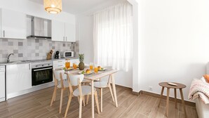 Una cocina moderna con armarios blancos, una mesa de comedor de madera y un taburete pequeño y redondo.
