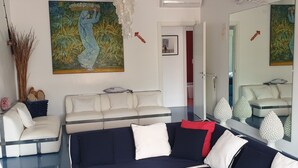 Un salon moderne avec un canapé d’angle, un canapé blanc et un grand tableau abstrait accroché au mur.