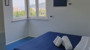 Une chambre d’hôtel avec une grande fenêtre, un lit avec une literie bleue et un petit téléviseur fixé au mur.