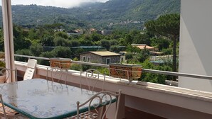 Un balcon avec une table et des chaises, donnant sur un paysage montagneux parsemé de maisons.