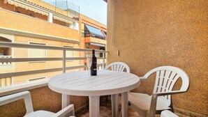 Un balcone con un tavolo rotondo e due sedie bianche, affaccia su un edificio con balconi.