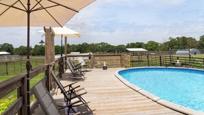 Terraza de madera con sillones de descanso y sombrillas con vistas a una piscina.