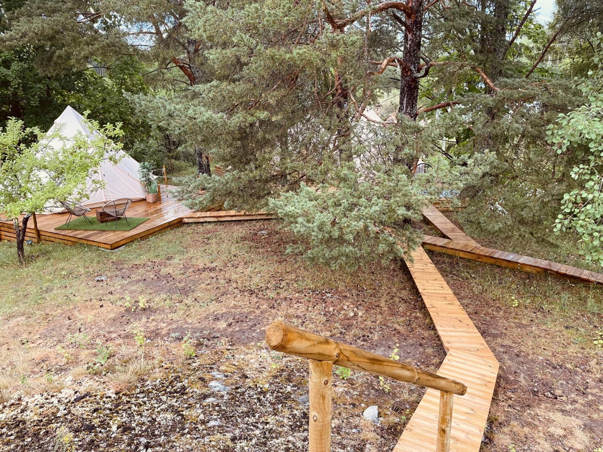 A wooden deck with a small wooden structure, surrounded by trees and a tent in the background.
