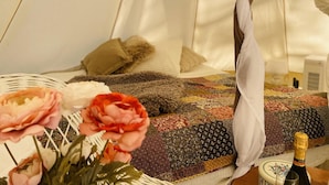 Una habitación acogedora con una cama, un dosel tejido, una colcha y una botella de champán.