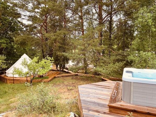 A wooden deck with a hot tub, surrounded by trees and a tent.