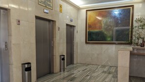 An elevator area with marble flooring, two elevators, trash bins, and a large abstract painting on the wall.
