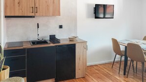 A compact kitchen with wooden cabinets, a built-in dishwasher, a small sink, and a dining area with a table and chairs.