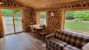 A cozy room with a stone wall, a wooden table with chairs, a plaid sofa, and a view of the outdoors. - The Forge at Torch Lake: near lake access and boat ramp, boat trailer parking (Central Lake)