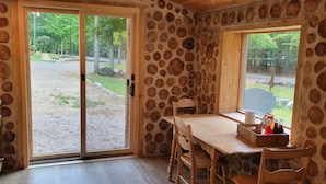A rustic room with a stone wall, a wooden table with chairs, a window, and a kitchen area with a stove. - The Forge at Torch Lake: near lake access and boat ramp, boat trailer parking (Central Lake)